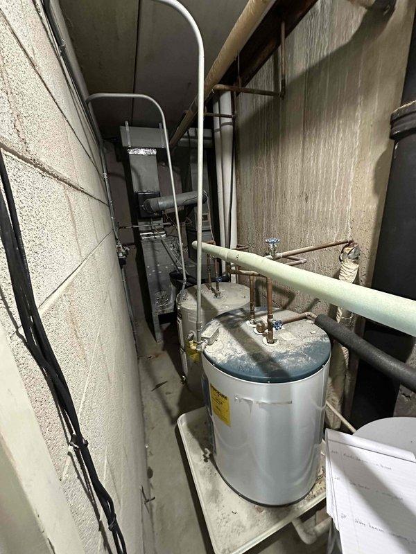 Conducted on-site assessment of existing HVAC air handler located in condo unit 22D closet for replacement estimate. Documented current equipment configuration including furnace/air handler unit, associated ductwork, water heater, and mechanical connections. Evaluated spatial constraints within the narrow utility closet, noting concrete block construction, existing copper and PVC piping infrastructure, electrical conduit routing, and duct connections to prepare comprehensive replacement specifications for proper equipment sizing and installation planning.