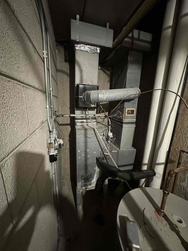 Conducted on-site assessment of existing HVAC air handler located in condo unit 22D closet for replacement estimate. Documented current equipment configuration including furnace/air handler unit, associated ductwork, water heater, and mechanical connections. Evaluated spatial constraints within the narrow utility closet, noting concrete block construction, existing copper and PVC piping infrastructure, electrical conduit routing, and duct connections to prepare comprehensive replacement specifications for proper equipment sizing and installation planning.