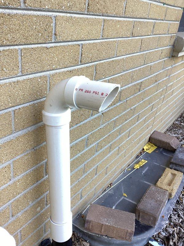 Completed warranty termination rework on exterior condensate drain system. Reinstalled PVC drain line assembly with proper 90-degree elbow configuration and secured vertical discharge pipe to exterior wall. Repositioned drain pan with stabilizing blocks at base to ensure proper condensate collection and verified all connections for leak-free operation.