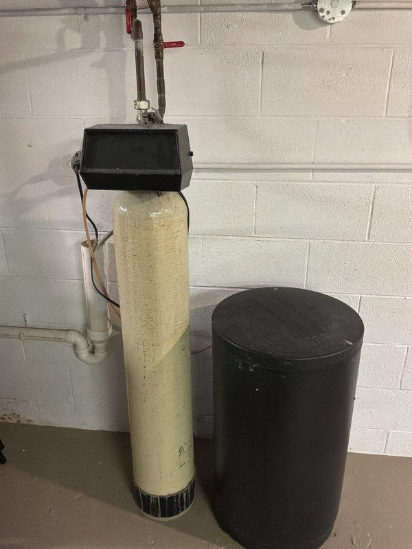Responded to service call for leaking water heater. Upon arrival, performed diagnostic inspection and confirmed active water leak from tanked water heater unit. Assessed condition of equipment and surrounding area, documenting water damage on basement floor near base of unit. Evaluated water heater for potential repair versus replacement, noting age and extent of leak. Photographed existing plumbing configuration including water softener system, brine tank, copper supply lines, and venting assembly for service records.