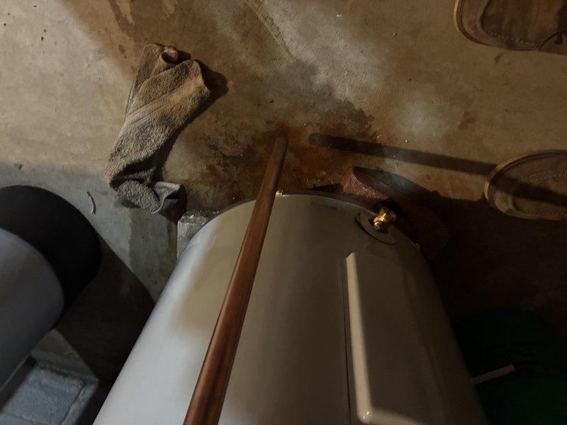Responded to service call for water heater leaking from pipe connections. Upon arrival, inspected tanked water heater and identified active leak at copper pipe compression fittings with blue plastic ferrules. Evidence of significant water damage was visible on floor surrounding unit, with extensive staining and discoloration indicating ongoing moisture issues. Assessed plumbing connections at top of water heater, noting corrosion on copper pipes and mineral deposits around connection points. Tightened compression fittings and verified proper seal at both inlet and outlet connections. Cleaned area and monitored for additional leakage to confirm repair effectiveness.