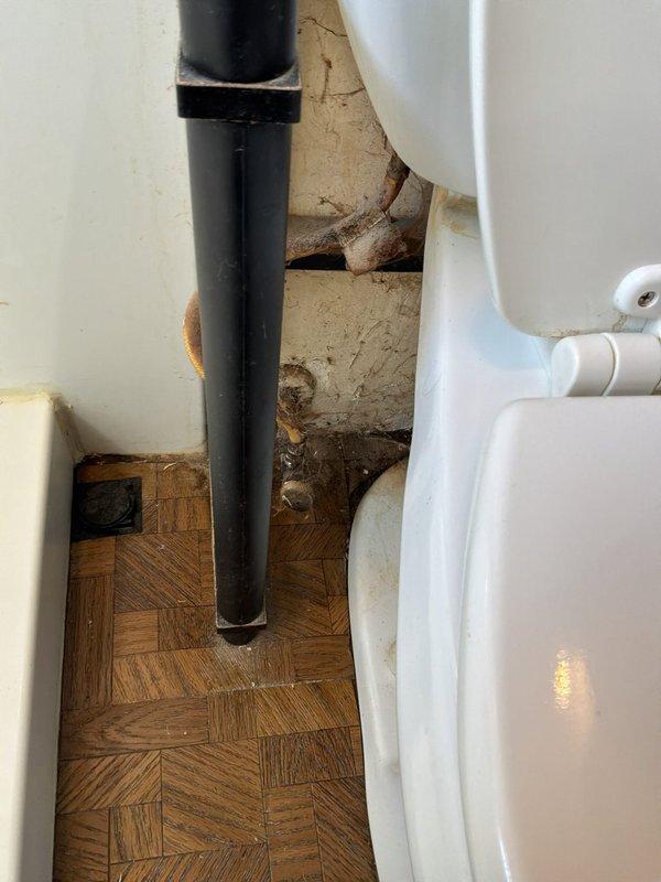 Provided estimate for toilet replacement in residential bathroom. Customer has new fixture ready for installation. Assessed existing toilet condition and surrounding plumbing connections, noting deteriorated wall surface behind unit with visible moisture damage, cracking, and paint failure. Documented water supply line configuration and floor conditions for replacement procedure.