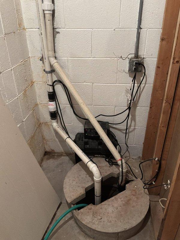 Conducted on-site evaluation of existing sump pump discharge system to provide estimate for installation of above-ground winter diverter assembly. Assessed current configuration including PVC discharge piping mounted along basement wall with proper bracketing, functional sump pump unit with dual pit covers, and electrical connections. Examined exterior discharge point where sump line exits foundation and terminates at lawn area adjacent to driveway to determine optimal diverter placement and routing requirements for seasonal drainage management. Documented basement installation and exterior discharge location with photographs for estimate preparation.