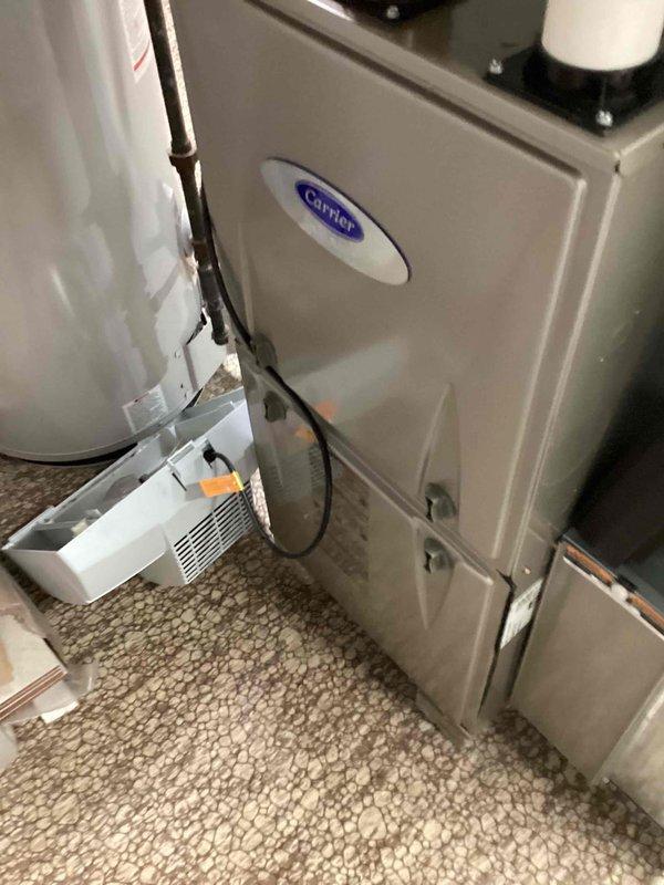 Performed a tune-up on a Carrier gas furnace, including inspection of the unit, vent piping, and condensate drain components. Used a digital manometer to check pressure readings during operation. Noted a displaced condensate pump/drain pan assembly near the unit and documented its condition for follow-up.