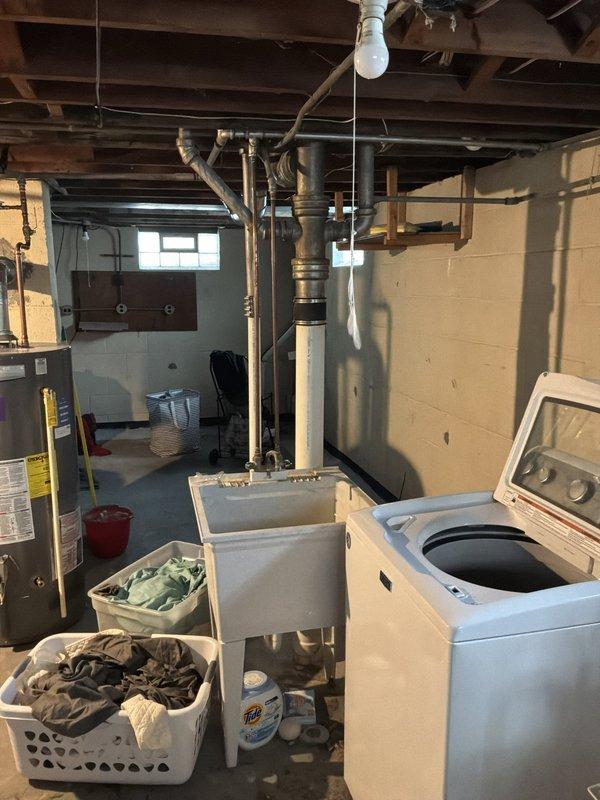 Performed a whole-home plumbing inspection, including the basement laundry area, water heater, utility sink, and visible drain, vent, and supply piping. Observed aged galvanized supply piping with surface corrosion and mineral buildup, washing machine supply valves and hoses, and staining on the foundation wall, with no active leaks or significant damage noted. Documented system conditions with photos and recommended monitoring the aging galvanized lines and supply hoses for future replacement.