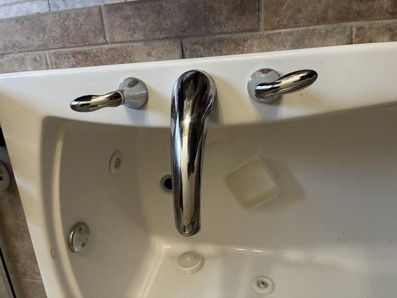 Re-caulked the kitchen sink perimeter to restore a watertight seal. Diagnosed dripping faucets at the master bathroom deck-mounted tub fixture and the guest bathroom fixture, inspecting the under-fixture brass compression supply connections and flexible supply lines for leaks and wear. The inspection also found corrosion on nearby hardware beneath the fixture.