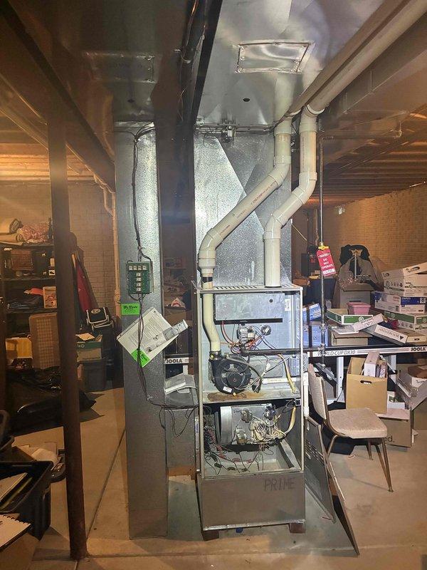 Performed an on-site evaluation for replacement of a 20+ year old natural gas furnace and matching air conditioning system, with the furnace located in the basement and previously shut down due to a failed heat exchanger. Inspected the furnace cabinet, burner and inducer assembly, control components, PVC venting, and existing ductwork transitions, noting corrosion near the inducer motor, and documented conditions with photos to prepare a same-day replacement estimate.