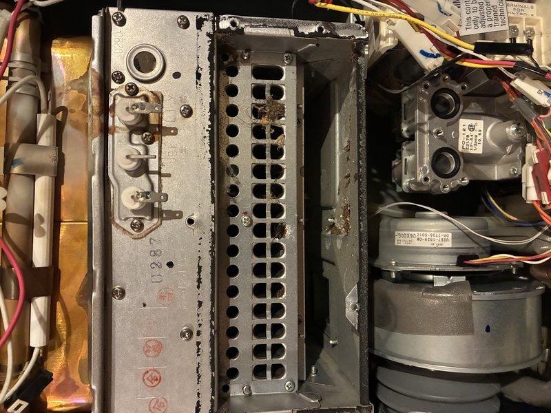 Diagnosed a gas-fired tankless water heater displaying error code 11 (ignition failure). Inspection of the burner compartment revealed heavy corrosion and rust debris on the burner assembly, flaking coating on the igniter/sensor bracket, and discoloration on the heat exchanger surfaces, indicating combustion and ignition reliability issues. Verified gas valve, blower, and wiring connections and documented findings with photos for repair recommendations.