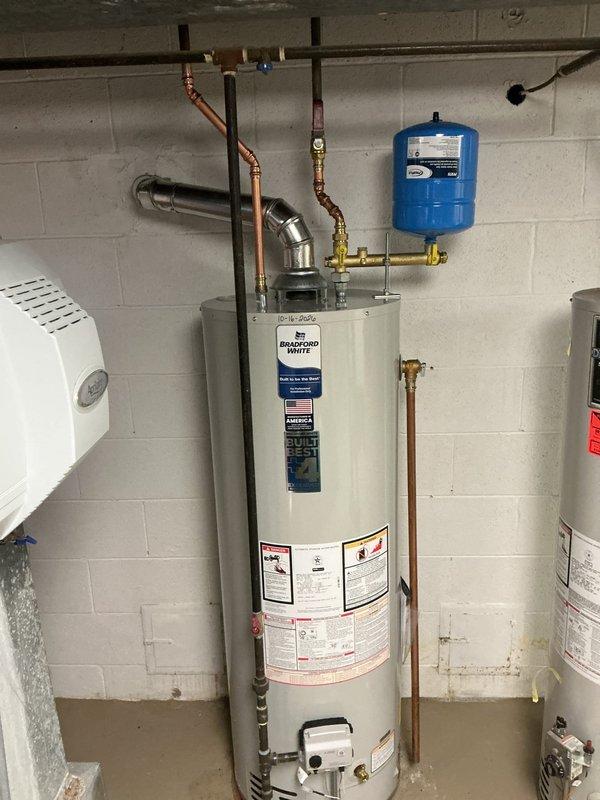 Installed a new 40-gallon natural gas Bradford White tall water heater, connecting the gas supply, domestic water lines, and flue vent to meet code requirements. Verified proper expansion tank mounting on the brass manifold fitting, confirmed all connections were secure, and left the manufacturer's BuiltBest+4 extended warranty registration information with the unit.