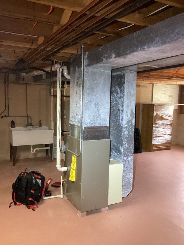 Responded to a reported furnace leak and performed a diagnostic inspection of the upright gas furnace, removing the front access panel to examine the inducer/blower assembly, burner compartment, gas valve, wiring, and control components. Inspected the PVC condensate drain piping and surrounding plenum and ductwork, noting chalky corrosion or residue buildup on the galvanized supply plenum consistent with moisture exposure, to identify the source of the leak.