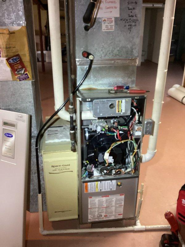 Responded to a reported furnace leak and performed a diagnostic inspection of the upright gas furnace, removing the front access panel to examine the inducer/blower assembly, burner compartment, gas valve, wiring, and control components. Inspected the PVC condensate drain piping and surrounding plenum and ductwork, noting chalky corrosion or residue buildup on the galvanized supply plenum consistent with moisture exposure, to identify the source of the leak.