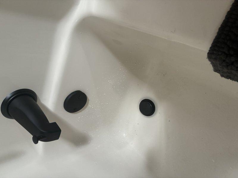 Removed and replaced the existing tub drain assembly, installing a new matte black overflow cover plate and drain stopper, and verified the diverter spout and drain operated properly. Also removed the worn, discolored shower arm and installed a new threaded shower arm at the wall connection, leaving the outlet ready for shower head attachment.