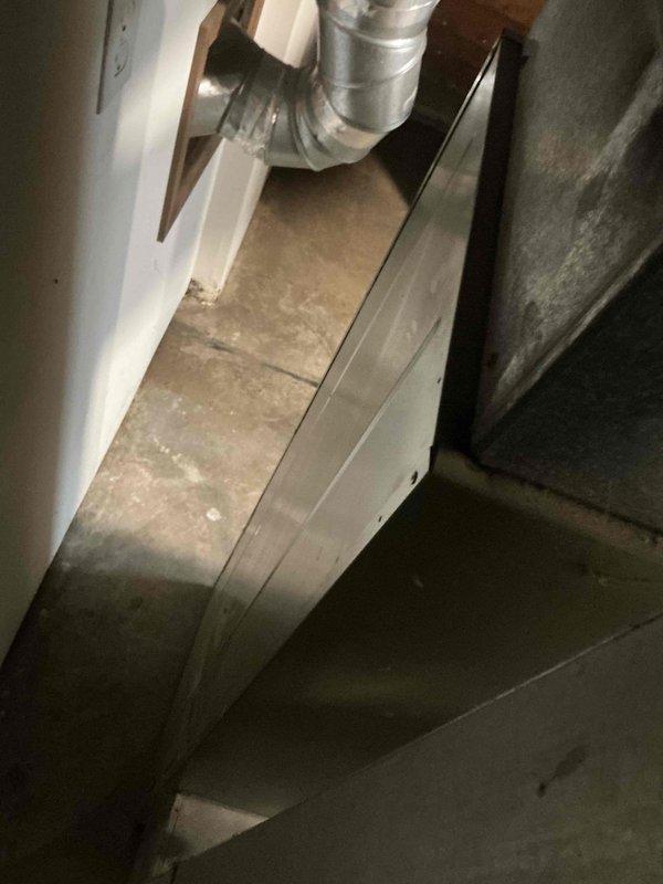 Performed an on-site replacement estimate for a 62-year-old Heil 80% AFUE natural gas upflow furnace, documenting the unit's condition, nameplate data, and surrounding galvanized supply/return ductwork and flue venting through the wall. Noted significant dust and debris accumulation inside the cabinet, aged and soiled equipment, and a stained, uneven concrete floor at the base of the unit. Documented the existing configuration to support sizing and replacement recommendations for a new high-efficiency furnace.