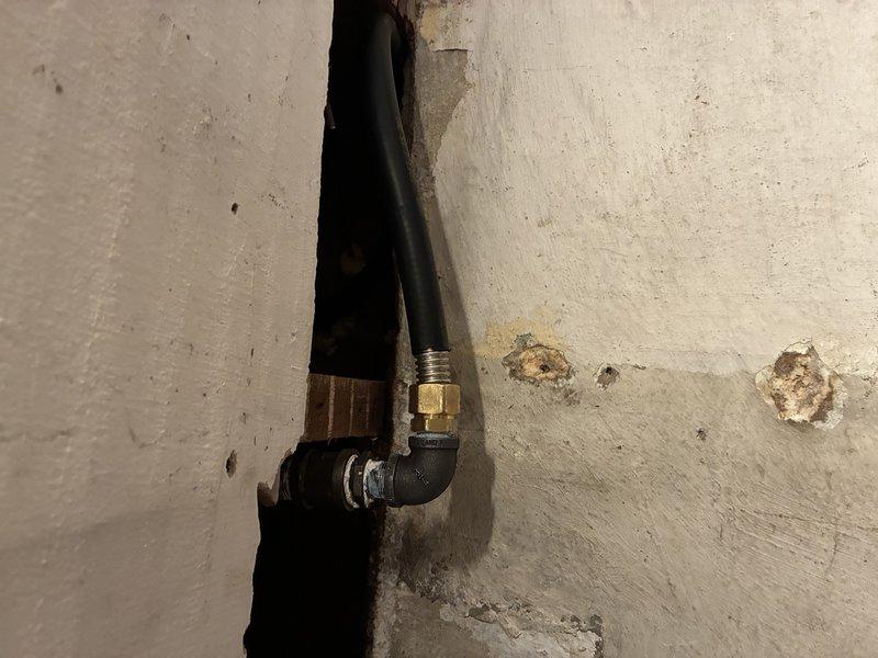Installed a 3/4" black iron gas line to the stove location, routed through the wall cavity and terminated with a brass fitting and elbow connection to a flexible appliance connector. Sealed the pipe penetration through the framing with foam sealant to close the opening around the line.