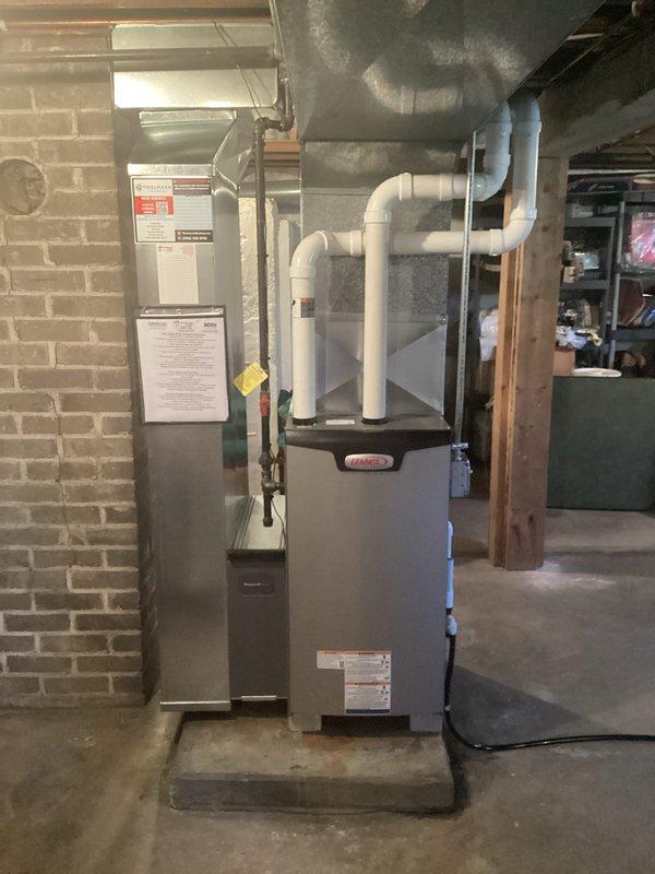 Installed a new Lennox gas furnace on a raised concrete pad in the basement, connecting the PVC intake/exhaust venting to the plenum and ductwork and tying into the existing black iron gas supply with a shutoff valve. Completed the electrical connections and condensate drain routing under permit, with a licensed electrician involved, then affixed the required rating and warning labels and posted contractor and maintenance information at the unit.