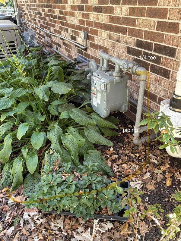 Performed an on-site estimate for a new natural gas line extension from the existing exterior meter to a pool heater. Inspected the meter and existing 1" gray galvanized piping along the brick wall, identified a 1-1/4" tee as the tie-in point, and documented a proposed pipe route across the landscaped bed with annotated photos. No corrosion or damage was observed at the meter or existing piping.