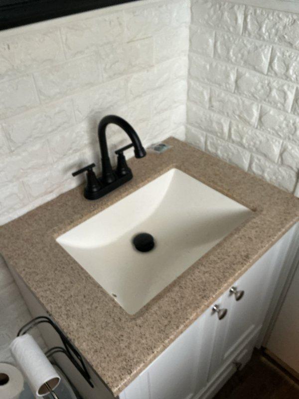 Installed a matte black two-handle, 8-inch widespread faucet with a matching pop-up drain assembly on the vanity's undermount sink, connecting the supply lines and drain and verifying proper flow and leak-free operation. Inspected the under-sink supply and shutoff valve connections, noting rust staining near the chrome supply fittings and valve, and checked the supply and drain connections for tightness. The jetted tub repair was identified as a separate item requiring further diagnosis.