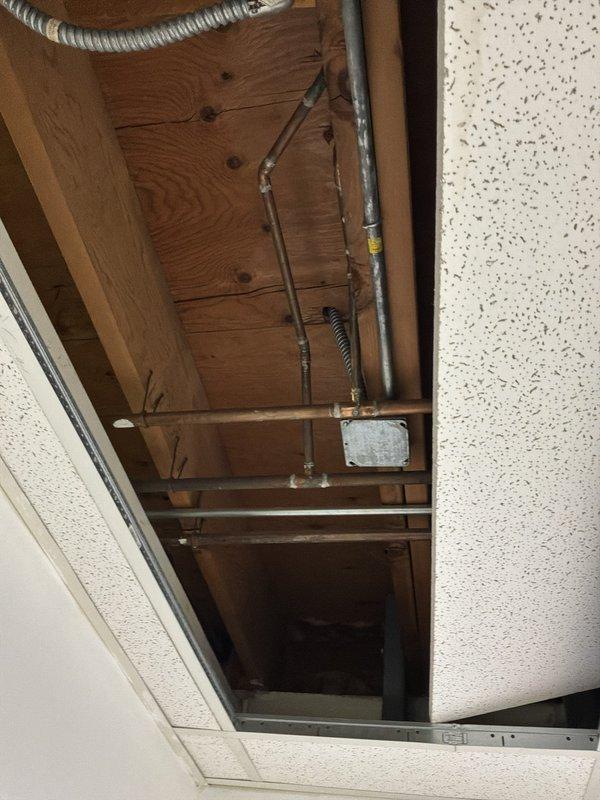 Performed an on-site assessment for installing a new gas line to a range, evaluating the existing overhead pathway above the drop ceiling and in the basement utility area. Inspected the exposed joist space and surrounding piping, conduit, and ductwork to identify a viable routing path and potential obstructions. Documented existing conditions with photos to support material takeoff and installation planning.