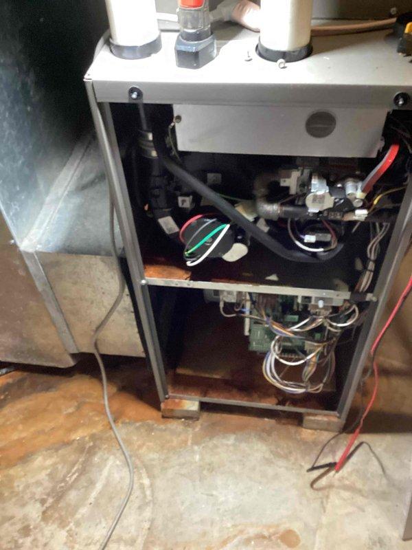 Diagnosed a no-heat complaint on a gas furnace where the inducer blower ran but the unit failed to proceed through its ignition sequence. Testing of the control circuit, pressure switch, and gas valve assembly was performed with meter leads installed, and heavy rust and corrosion were found on the cabinet floor, burner compartment shelf, and base, with moisture staining on the surrounding concrete indicating a water or condensate leak. Findings were documented with photos, and the moisture source and corrosion damage should be addressed to prevent further component failure.