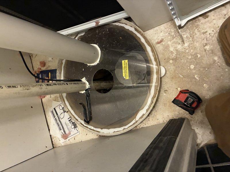Assessed the existing sump system, which includes a submersible primary pump with a float switch in a lined basin set in a concrete floor, a PVC discharge line, and a sealed basin cover with pipe penetrations. Evaluated the setup for the installation of a battery-powered backup sump pump to provide redundancy, and noted the basin condition, discharge routing, and sealant at the cover and rim as considerations for the proposed work.