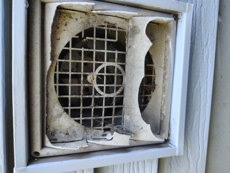 Inspected the exterior wall vent serving the customer's Broan-NuTone ventilation system and found the plastic cover severely cracked and broken, with the wire grille exposed and heavily coated in dirt and debris. Verified the associated flexible and rigid galvanized ductwork in the joist bays and found no significant damage, then evaluated replacement options for the 8"x8" opening to restore proper exterior exhaust termination.