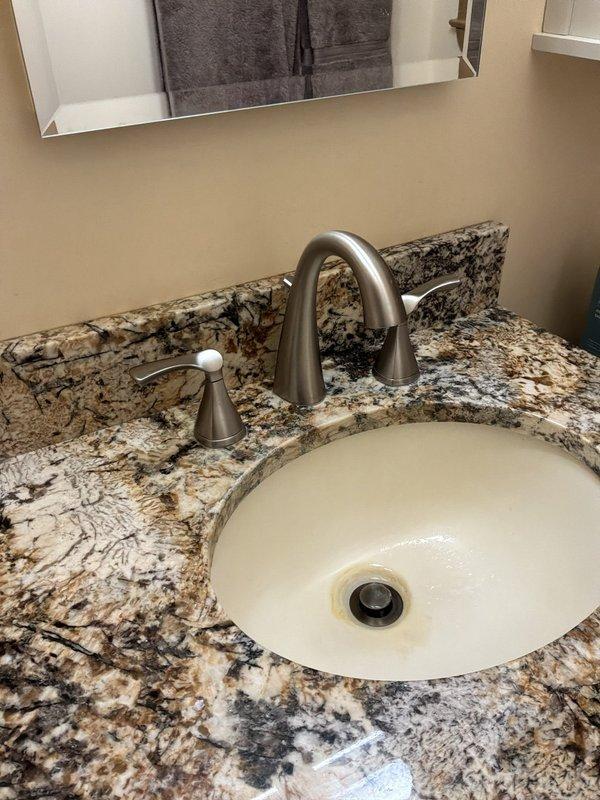 Inspected the bathroom vanity and evaluated the plugged faucet spout, the bathroom fixture shutoff valves, and several outdoor faucets requiring new gaskets. The angle-stop valves and braided supply lines beneath the sink showed no visible leaks or corrosion, and the drain assembly appeared intact, with mineral staining noted around the basin drain. Scope of work was assessed for the spout clearing, shutoff valve service, and outdoor faucet gasket replacement.