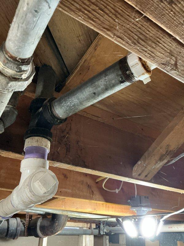 Diagnosed a leak at a corroded galvanized section of the waste stack, where rust staining was found at a slip-joint nut fitting near the sanitary tee and transition coupling to PVC drain piping. Inspected the adjacent cast iron drain lines, hub couplings, and cleanout for additional deterioration or seepage, and documented the affected fittings to support recommended repair of the failing galvanized waste components.