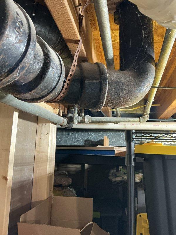 Diagnosed a leak at a corroded galvanized section of the waste stack, where rust staining was found at a slip-joint nut fitting near the sanitary tee and transition coupling to PVC drain piping. Inspected the adjacent cast iron drain lines, hub couplings, and cleanout for additional deterioration or seepage, and documented the affected fittings to support recommended repair of the failing galvanized waste components.