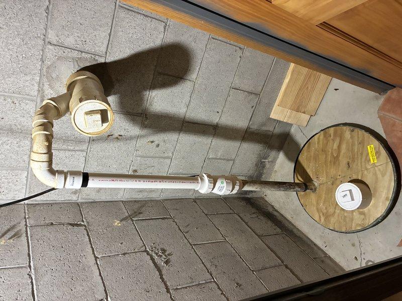Performed a diagnostic inspection of the sump pump system, which had not been previously serviced, to verify operational condition. Inspected the discharge piping assembly, including the cleanout wye, PVC couplings, and the transition to the rusted pipe section at the sump basin cover, and observed the pit interior and flexible corrugated connection for obstruction or defects. Documented corrosion and buildup on the fittings and recommended further evaluation or maintenance as needed to ensure reliable operation.