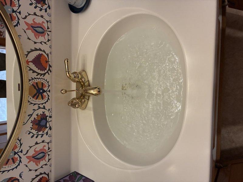 Responded to a slow-draining bathroom vanity sink and inspected the drain assembly, including the chrome tailpiece, slip-joint connection, and PVC P-trap, to clear the restriction and restore proper flow. Verified drainage by running water through the basin, and noted corrosion on the floor-penetration flanges and supply shutoff escutcheons under the cabinet for future monitoring.