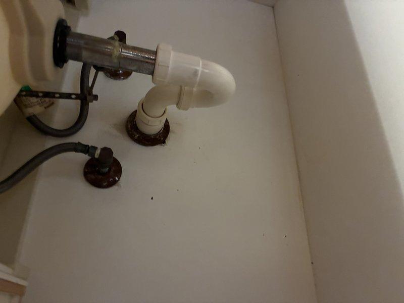 Responded to a slow-draining bathroom vanity sink and inspected the drain assembly, including the chrome tailpiece, slip-joint connection, and PVC P-trap, to clear the restriction and restore proper flow. Verified drainage by running water through the basin, and noted corrosion on the floor-penetration flanges and supply shutoff escutcheons under the cabinet for future monitoring.