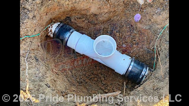 Pride Plumbing came out and dug down in the yard to expose and access the outside main sewer septic drain line, cut into the line, installed two new two-way PVC cleanouts with caps (connecting them to the existing outside main sewer septic drain line with new PVC fittings and Fernco couplings), covered the area we dug up after installation, and added concrete collars around the cleanout caps.