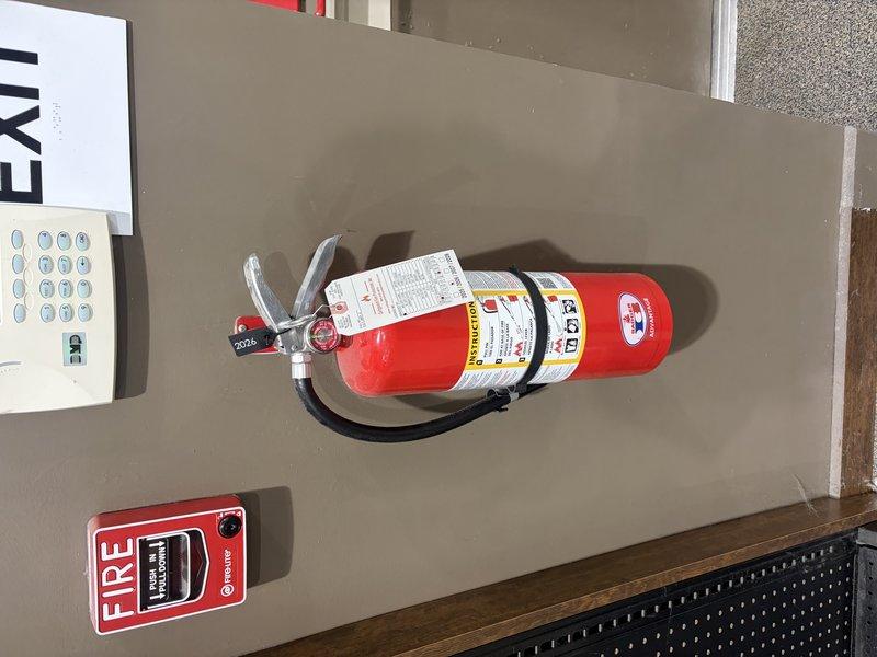 Completed annual fire extinguisher inspection at commercial facility. Inspected two fire extinguishers for compliance with NFPA standards, verifying proper pressure levels, pin and tamper seal integrity, hose condition, and label legibility. Confirmed both units were properly mounted with appropriate signage and accessibility. One ABC-type extinguisher located in retail area on floor level and one wall-mounted unit near exit with accompanying fire signage. All extinguishers passed visual inspection with no deficiencies noted. Updated inspection tags to reflect current service date.