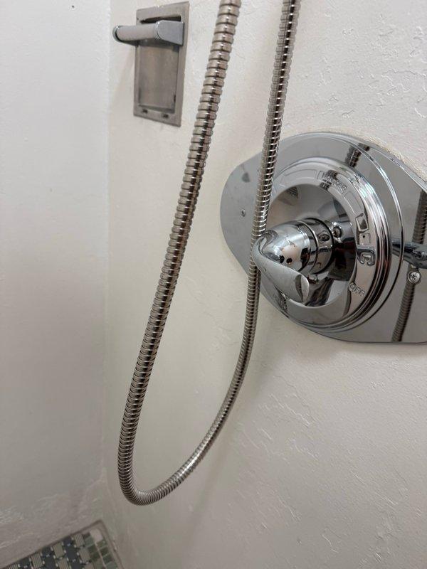 Performed diagnostic evaluation of bathroom shower system and accessed plumbing infrastructure through wall cavity. Inspected thermostatic shower valve assembly with chrome finish, verified proper installation of dual flexible metal supply hoses, and documented existing fixture configuration. Opened wall access point to examine copper supply lines, associated mechanical systems, and structural components to assess scope of work outlined in estimate.