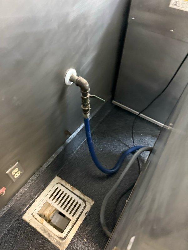 Responded to diagnostic service call for commercial kitchen plumbing evaluation. Upon arrival, inspected two-compartment stainless steel utility sink with wall-mounted hand washing station, noting visible PVC drain connections and wall-mounted spray hose assembly. Examined floor-level plumbing components including scattered brass fittings and white perforated floor drain cover positioned near sink area. Assessed secondary service area where blue rubber supply line connects to wall-mounted fitting with metallic elbow connector approximately twelve inches above floor level. Documented existing plumbing configuration and equipment conditions through photographic records for future reference and scope determination. All observations recorded for further evaluation and repair recommendations.