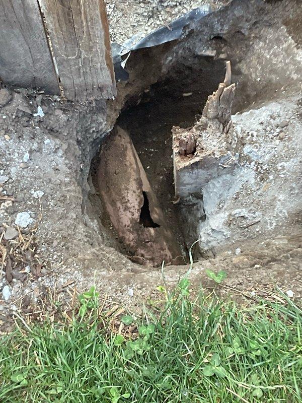 Responded to emergency call regarding damaged clay sewer drain line in backyard. Homeowner had discovered previous owner installed fence post with concrete footing directly over the drain line, which broke during post removal, leaving the line open to atmosphere. Conducted thorough diagnostic assessment of the affected area, including inspection of the exposed clay pipe beneath the structure's foundation and documentation of the extent of damage. Evaluated the corroded condition of existing drainage infrastructure and compromised foundation access point. Photographed damage to crawl space area showing deteriorated concrete, exposed soil cavity, and heavily corroded piping. Assessed structural impact to foundation walls and documented debris field from concrete removal. Provided homeowner with professional assessment of repair options and recommended course of action to restore proper drainage function and seal the compromised sewer line.