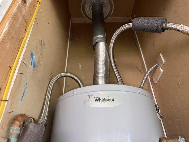 Provided estimate for replacement of 30-gallon natural gas water heater in manufactured home closet with dimensions of 23" x 23-1/2" x 72". Existing Whirlpool/US Craftmaster unit (30,000 BTU/HR, approximately 16-1/2" x 60") showing active leak at cold water inlet valve connection between hard line and braided stainless supply line. Water damage observed on particle board flooring beneath unit requiring replacement with plywood. Assessed space constraints and provided pricing comparison for both 30-gallon and 40-gallon replacement options. Documented existing installation configuration including flexible braided supply lines, venting system, and tight clearance conditions. Photographed current setup showing water heater positioning, plumbing connections, and surrounding structural framework for estimate preparation.