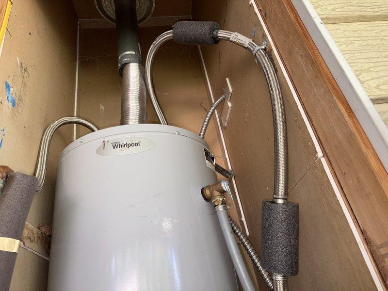 Provided estimate for replacement of 30-gallon natural gas water heater in manufactured home closet with dimensions of 23" x 23-1/2" x 72". Existing Whirlpool/US Craftmaster unit (30,000 BTU/HR, approximately 16-1/2" x 60") showing active leak at cold water inlet valve connection between hard line and braided stainless supply line. Water damage observed on particle board flooring beneath unit requiring replacement with plywood. Assessed space constraints and provided pricing comparison for both 30-gallon and 40-gallon replacement options. Documented existing installation configuration including flexible braided supply lines, venting system, and tight clearance conditions. Photographed current setup showing water heater positioning, plumbing connections, and surrounding structural framework for estimate preparation.