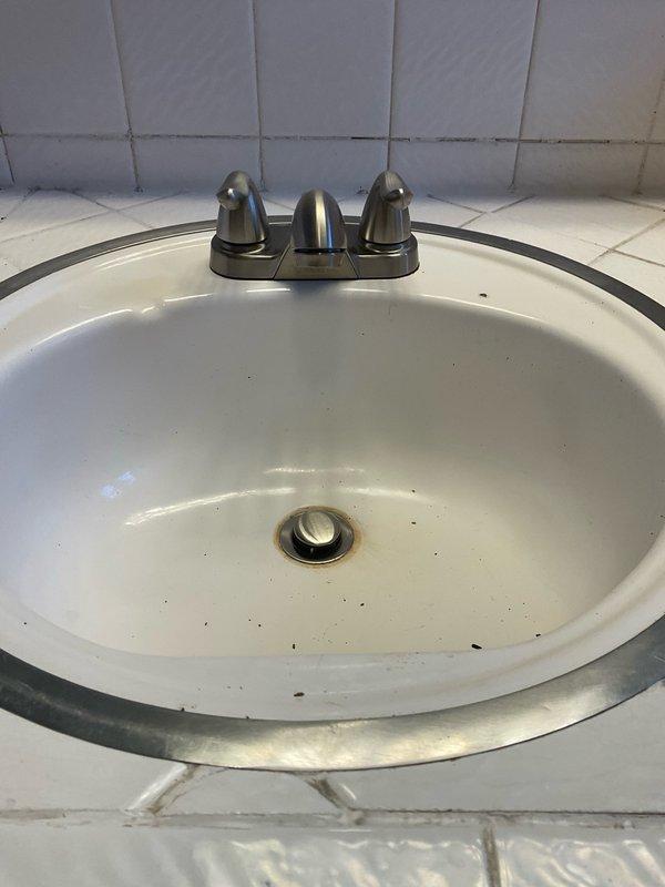 Conducted on-site assessment of bathroom fixtures requiring replacement. Evaluated existing two-handle faucet installation on oval porcelain sink basin with visible wear and staining. Inspected mounting configuration and existing supply line connections beneath vanity. Documented current fixture conditions including faucet hardware, shutoff valve accessibility, and drain assembly. Assessed second faucet location and toilet installation requirements. Photographed all fixtures and surrounding areas to prepare accurate material installation estimate for customer-supplied replacement components including two faucets, shutoff valves, and toilet assembly.
