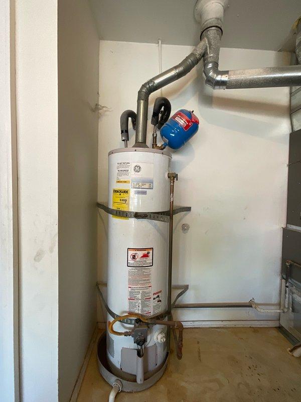 Responded to service call for non-operational gas water heater at rental property. Conducted on-site inspection and assessment of existing GE brand tanked gas water heater unit, documenting current installation configuration including venting system, gas line connections, expansion tank, safety strapping, and all associated plumbing connections. Photographed equipment and provided estimate for water heater replacement to property owner for approval.