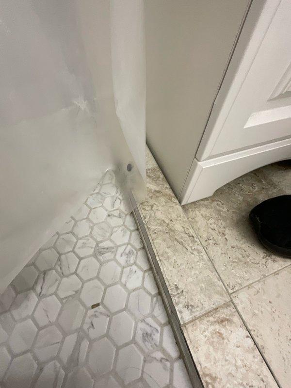 Responded to reported water leak in downstairs bedroom suspected to originate from upstairs bathroom sink. Upon arrival, conducted visual inspection of affected areas including hallway access point and upstairs bathroom. Examined flooring, walls, and plumbing fixtures in bathroom area where hexagonal tile flooring meets shower enclosure with glass door track system. Inspected sink drain connections, supply lines, and surrounding cabinetry for signs of active leakage or moisture intrusion. Documented conditions with photographs for diagnostic purposes. Advised homeowner of findings and recommended monitoring for additional leak activity to pinpoint exact source location.