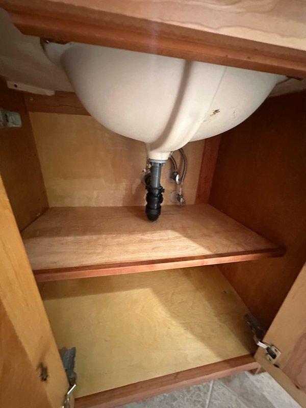 Responded to complaint of strong sewer smell from bathroom sinks. Performed diagnostic inspection of vanity cabinet and plumbing system beneath sink. Inspected drain assembly, P-trap configuration, and waste line connections for proper installation and potential defects. Documented plumbing conditions with photographs showing water supply lines, shut-off valves, drain piping, and cabinet interior for further assessment and recommended repairs.