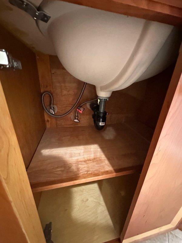 Responded to complaint of strong sewer smell from bathroom sinks. Performed diagnostic inspection of vanity cabinet and plumbing system beneath sink. Inspected drain assembly, P-trap configuration, and waste line connections for proper installation and potential defects. Documented plumbing conditions with photographs showing water supply lines, shut-off valves, drain piping, and cabinet interior for further assessment and recommended repairs.