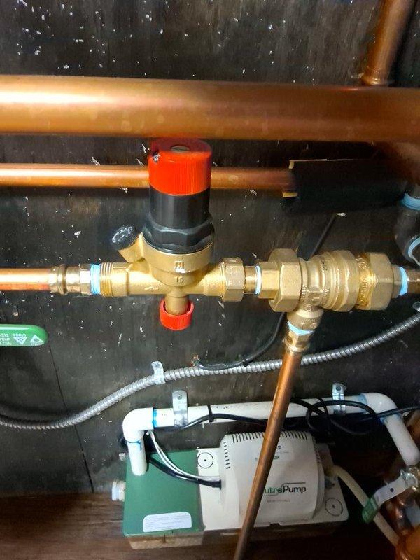 Responded to no hot water call with error code displaying on boiler. Upon arrival, inspected the heating system and identified issues with the boiler operation. Photographed the existing plumbing configuration, including the NeutraPump condensate removal system with PVC drainage connections, copper supply lines, and electrical connections. Also documented the pressure regulator assembly with brass valve body, red adjustment controls, and associated copper piping network. Troubleshot the error code, performed necessary diagnostics on the boiler and related components, and restored hot water service to the property.