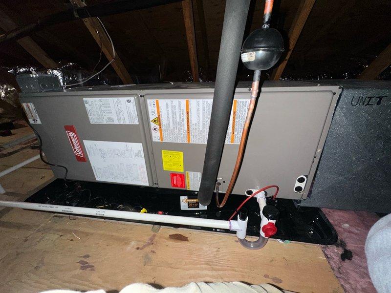 Completed installation of Coleman air handler unit in attic space, positioning equipment on wooden platform and securing all mounting connections. Connected refrigerant lines with protective covering, installed PVC condensate drain system with safety pan and valve controls, and verified proper integration of ductwork with reflective insulation barriers per manufacturer specifications.