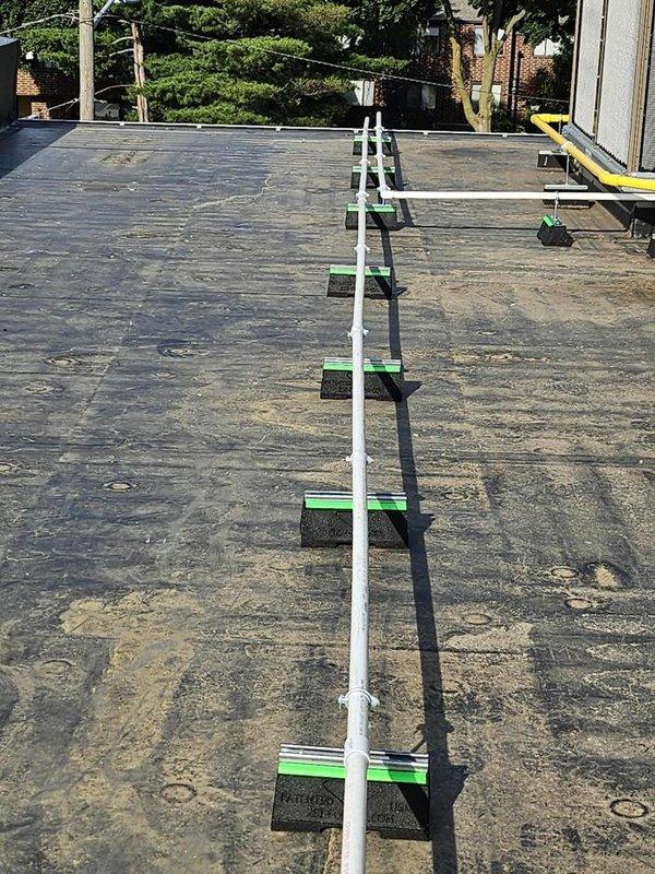 Extended drain lines for rooftop HVAC units using white PVC piping with properly spaced green support blocks to elevate and secure the lines above the roof membrane. Installation completed with appropriate mounting brackets to ensure proper drainage slope and prevent ponding while protecting the existing roof surface from damage.