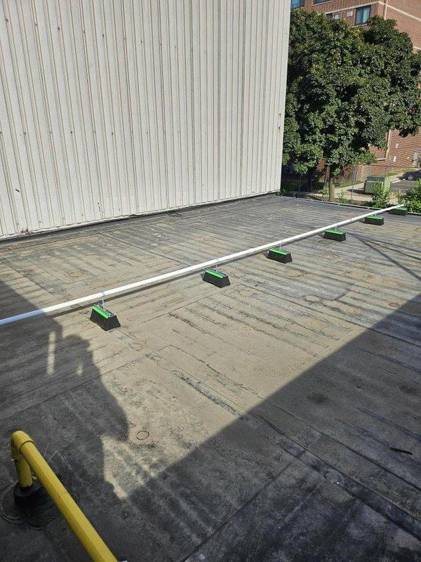 Extended drain lines for rooftop HVAC units using white PVC piping with properly spaced green support blocks to elevate and secure the lines above the roof membrane. Installation completed with appropriate mounting brackets to ensure proper drainage slope and prevent ponding while protecting the existing roof surface from damage.