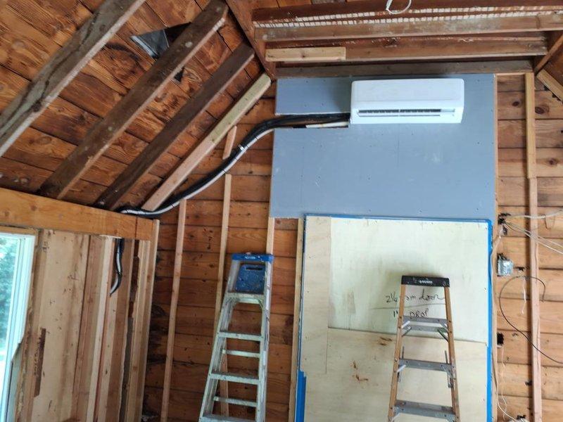 Completed installation of wall-mounted mini-split air conditioning unit in rear office area of structure undergoing renovation. Mounted indoor evaporator unit on prepared wall section with proper backing, routed refrigerant lines and electrical conduit through exposed framing to exterior, and secured all penetrations. Installation performed in active construction environment with exposed wooden framing and required coordination around ongoing finish work.