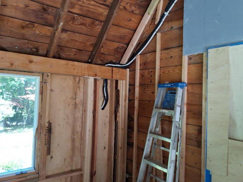 Completed installation of wall-mounted mini-split air conditioning unit in rear office area of structure undergoing renovation. Mounted indoor evaporator unit on prepared wall section with proper backing, routed refrigerant lines and electrical conduit through exposed framing to exterior, and secured all penetrations. Installation performed in active construction environment with exposed wooden framing and required coordination around ongoing finish work.