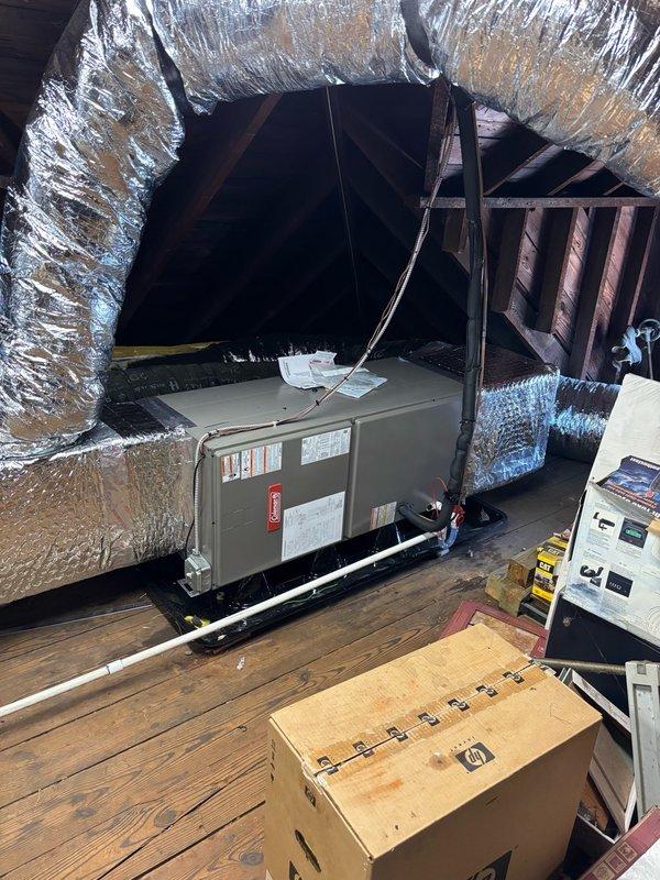 Completed installation of HVAC unit in second-floor attic space on right side of structure. Unit was positioned on proper support platform with all manufacturer specifications verified and labeled components clearly visible. Flexible aluminum ductwork was routed throughout the attic space to connect the new system, with insulated ducts extending from the unit to distribute conditioned air. Electrical control panel was mounted and wired to wall, featuring all necessary switches and control mechanisms for system operation. All ductwork was properly insulated with foil-faced reflective material to maximize energy efficiency and prevent condensation. System connections were secured, and installation was completed in accordance with manufacturer guidelines and industry standards.